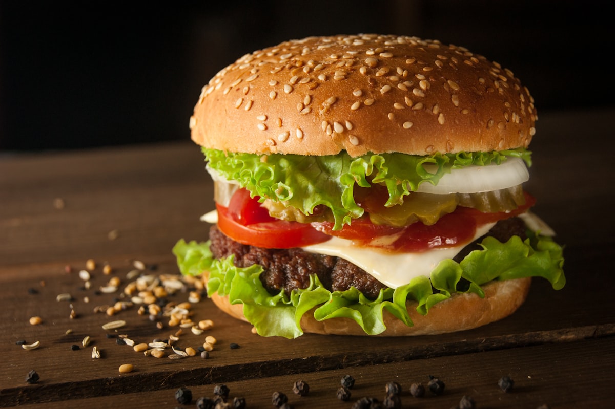 Cheeseburger mit Cheddar, Salat, Tomaten und Essiggurke im Sesambun